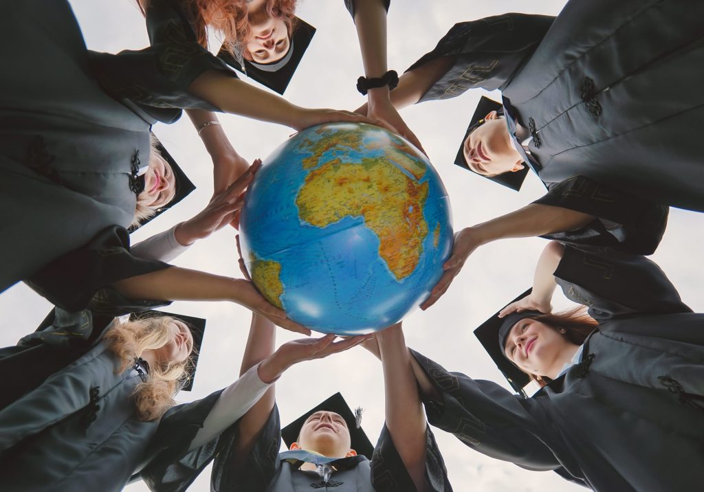 Graduating students twirl a geographic globe of the world in their hands.